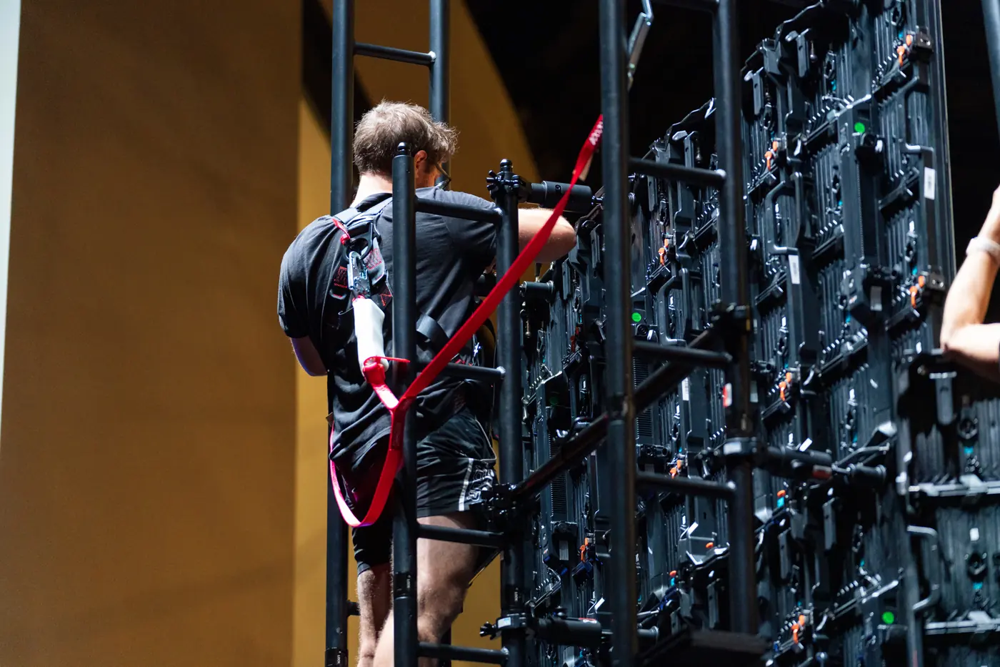 Crew member on a ladder at the rear of an LED wall showing tile access and cabling